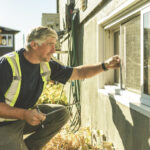 A professional technician in a high-visibility vest examines a window screen during a pest control inspection: what to expect when a specialist checks entry points around a home's exterior.
