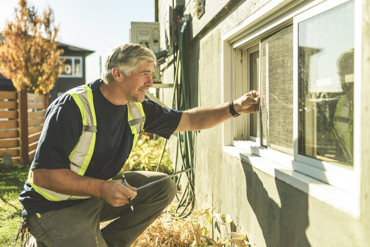A professional technician in a high-visibility vest examines a window screen during a pest control inspection: what to expect when a specialist checks entry points around a home's exterior.