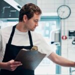 Restaurant employee completing a pest control checklist for restaurants while inspecting a commercial kitchen.