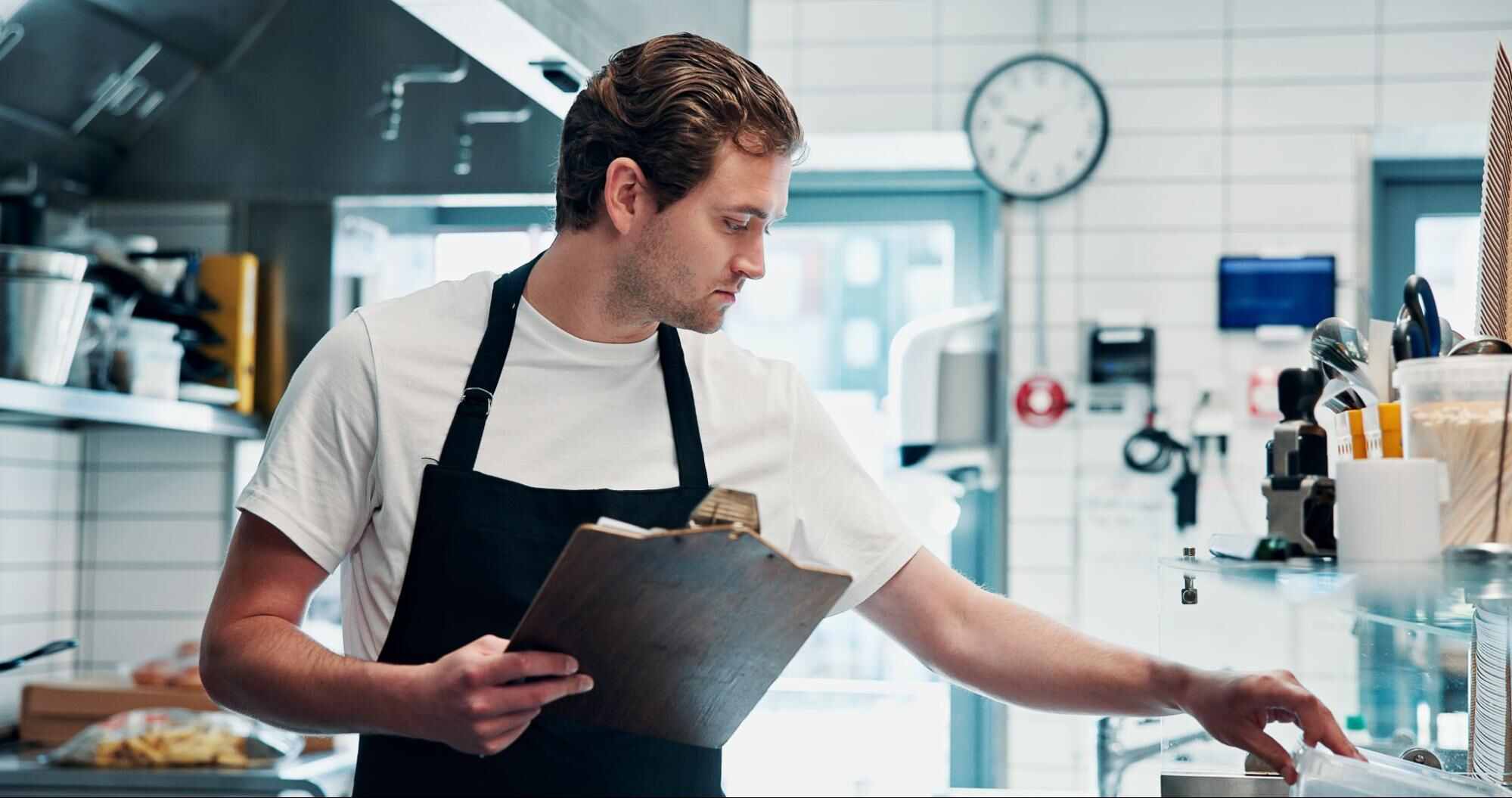 Restaurant employee completing a pest control checklist for restaurants while inspecting a commercial kitchen.